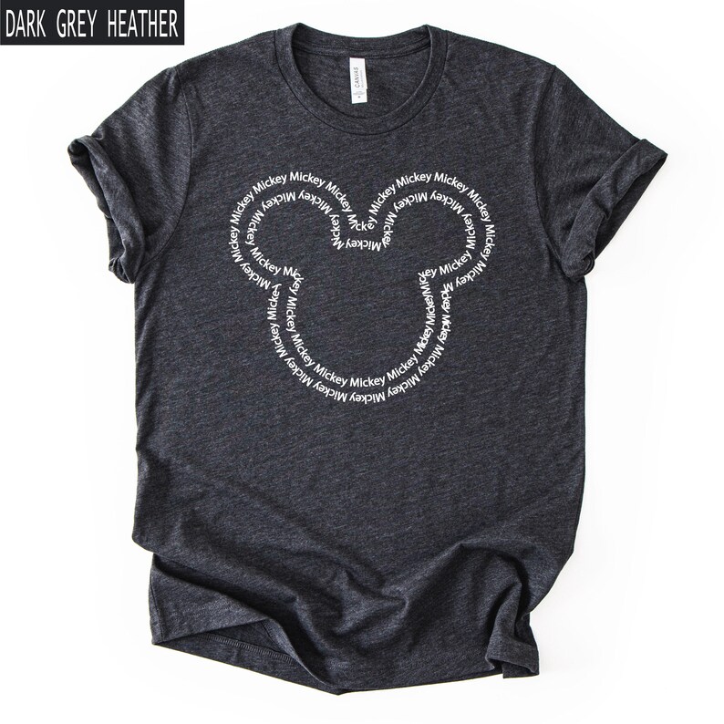 Peut inclure: T-shirt gris fonc&eacute; chin&eacute; avec un motif de t&ecirc;te de Mickey Mouse blanc. Le motif est compos&eacute; du mot "Mickey" r&eacute;p&eacute;t&eacute; en cercle. Le t-shirt est fait d'une mati&egrave;re douce et confortable.