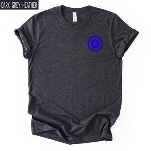 Pu&ograve; includere: T-shirt grigio scuro m&eacute;lange con grafica circolare blu sul petto. La grafica presenta una stella blu all'interno di un cerchio blu. Il testo "DARK GREY HEATHER" &egrave; in un rettangolo bianco nell'angolo in alto a sinistra.
