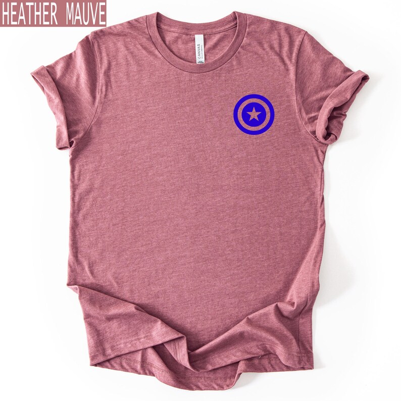 Pu&ograve; includere: T-shirt color malva melange con un disegno a scudo blu e beige sul petto. La maglietta &egrave; a girocollo e ha le maniche arrotolate. Il testo "HEATHER MAUVE" si trova nell'angolo in alto a sinistra.