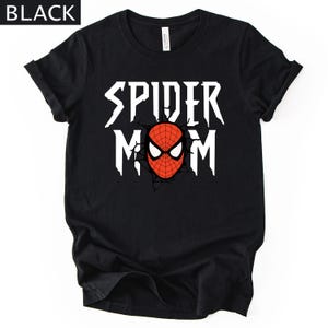 May include: Black t-shirt with the text "SPIDER MOM" in white, featuring a red and black spider-man mask graphic. The shirt has rolled-up sleeves and a crew neck.