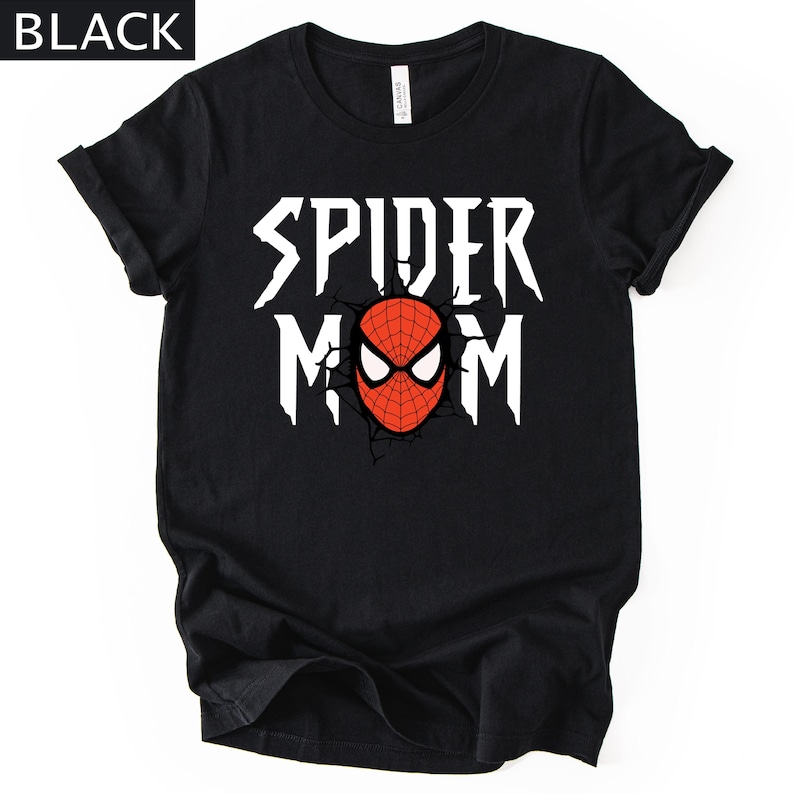 May include: Black t-shirt with the text "SPIDER MOM" in white, featuring a red and black spider-man mask graphic. The shirt has rolled-up sleeves and a crew neck.