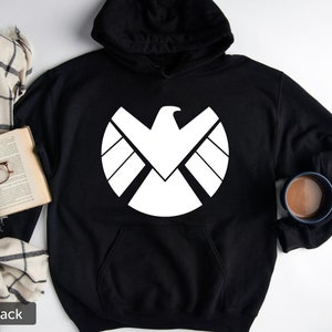 Puede incluir: Sudadera con capucha negra con un gr&aacute;fico blanco del logotipo de S.H.I.E.L.D.