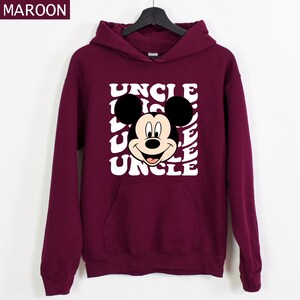 Pu&ograve; includere: Felpa con cappuccio color bordeaux con una grafica di Topolino e la parola "UNCLE" ripetuta in bianco con un font retr&ograve;. La felpa ha una tasca frontale e un cappuccio con coulisse. La parola "MAROON" &egrave; nell'angolo in alto a sinistra.