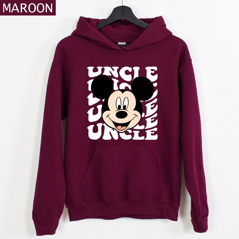 Pu&ograve; includere: Felpa con cappuccio color bordeaux con una grafica di Topolino e la parola "UNCLE" ripetuta in bianco con un font retr&ograve;. La felpa ha una tasca frontale e un cappuccio con coulisse. La parola "MAROON" &egrave; nell'angolo in alto a sinistra.