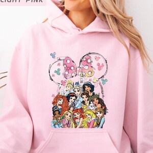 以下が含まれることがあります： ディズニーのプリンセスが描かれたライトピンクのパーカー。デザインにはミニーマウスのリボンと、アニメのプリンセスキャラクターのコレクションが含まれています。パーカーは柔らかい素材でできており、ドローストリングフードが付いています。