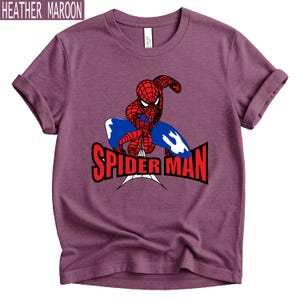 Op de afbeelding: Heather maroon t-shirt met een rood en blauw Spider-Man-ontwerp en de tekst "SPIDER MAN" in het rood. Het shirt heeft opgerolde mouwen en een ronde hals. De tekst "HEATHER MAROON" staat bovenaan.