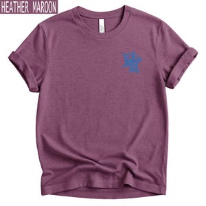 Op de afbeelding: Een heather maroon t-shirt met korte mouwen, een ronde hals en opgerolde mouwen. Het shirt heeft een kleine, blauwe lijntekening van een schedel op de linkerborst. De stof heeft een zichtbare gem&ecirc;leerde textuur.