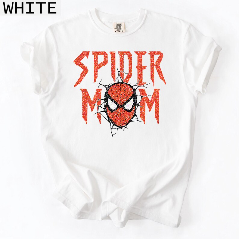 May include: White t-shirt with the words "SPIDER MOM" in red glitter lettering. The design includes a red and black glitter Spider-Man mask. The shirt is a casual, everyday wear item.