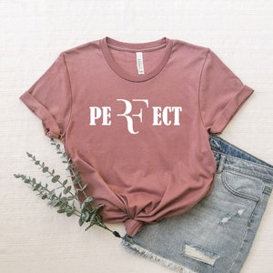 Op de afbeelding: Een mauve t-shirt met een witte afbeelding waarop "PERFECT" staat met een gestileerde "R" in het midden.