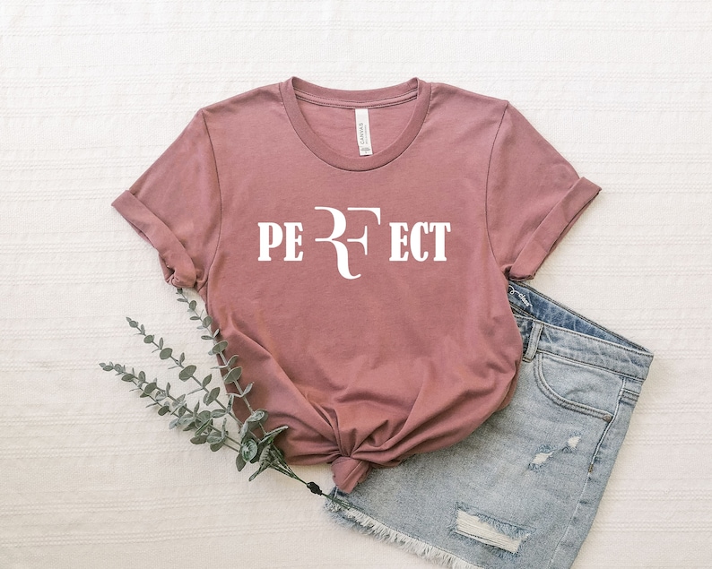 Op de afbeelding: Een mauve t-shirt met een witte afbeelding waarop "PERFECT" staat met een gestileerde "R" in het midden.