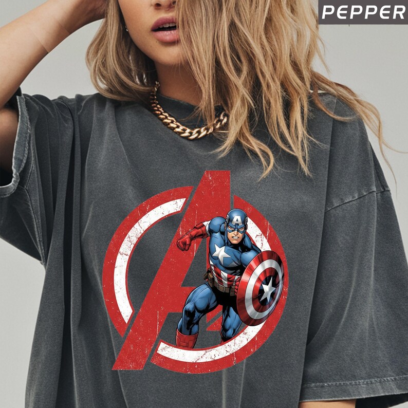 Puede incluir: Camiseta gris oscuro con el logotipo de los Vengadores desgastado y el Capit&aacute;n Am&eacute;rica. La camiseta tiene un aspecto vintage. La palabra "PEPPER" est&aacute; impresa en la esquina superior derecha.