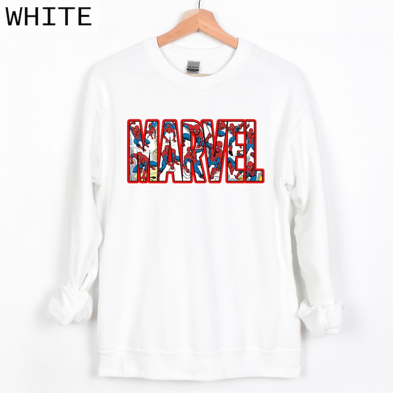 Puede incluir: Sudadera blanca con la palabra "MARVEL" en letras rojas. Las letras est&aacute;n rellenas de im&aacute;genes de Spider-Man con su cl&aacute;sico traje rojo y azul. La palabra "WHITE" est&aacute; en la esquina superior izquierda.