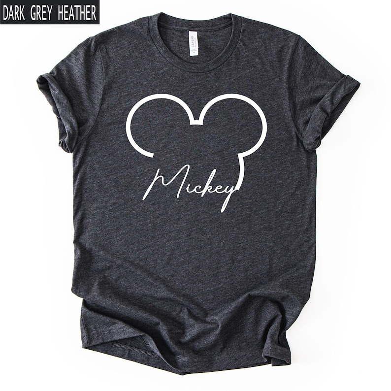May include: Dark grey heather t-shirt with a white outline of Mickey Mouse ears and the name "Mickey" in a cursive font. The shirt has rolled-up sleeves and a crew neck.