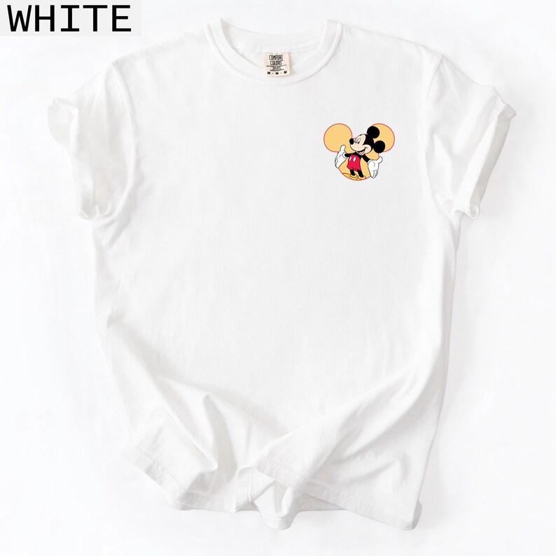 May include: White t-shirt featuring a small Mickey Mouse graphic on the chest. The cartoon character is shown in his classic outfit with yellow ears, a red jacket, and white gloves. The word "WHITE" is printed in black at the top.