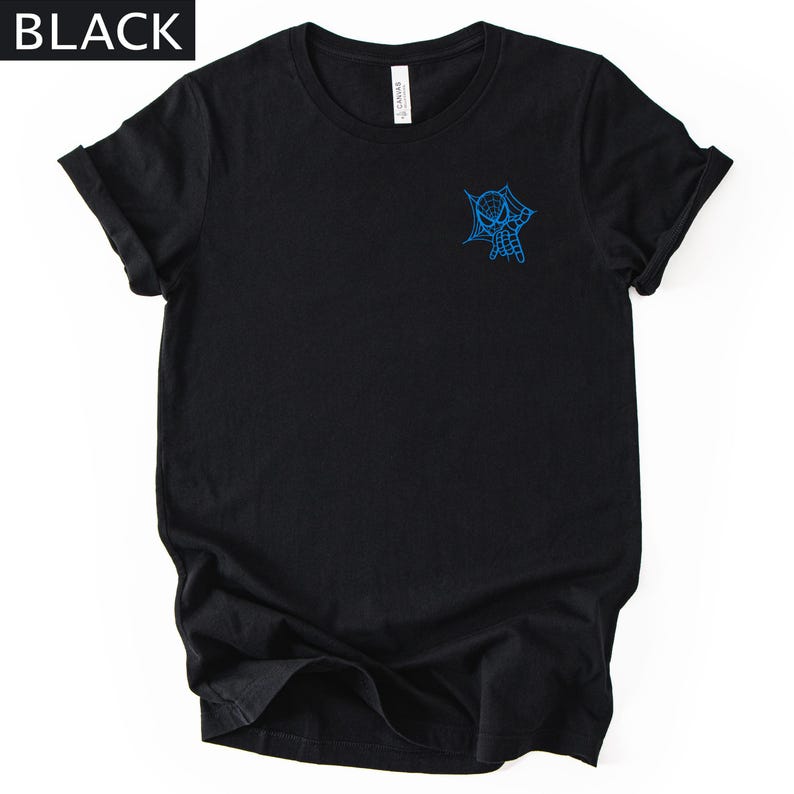 Op de afbeelding: Een zwart T-shirt met korte mouwen en een kleine blauwe afbeelding op de linkerborst. De afbeelding toont een karaktermasker dat uit een spinnenwebontwerp tevoorschijn komt. Het woord BLACK staat in de linkerbovenhoek van de afbeelding.