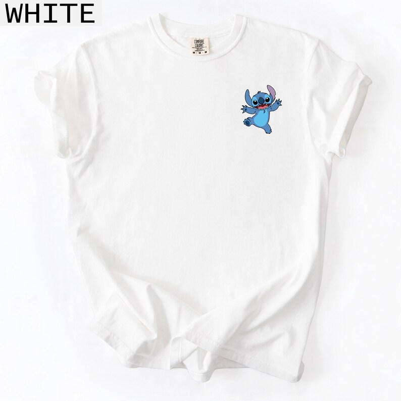 May include: White t-shirt featuring a small graphic of the character Stitch from the animated film Lilo & Stitch. The blue Stitch is in a playful pose with arms outstretched. The word "WHITE" is printed in black at the top of the image.