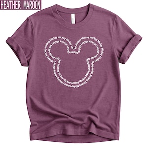 Peut inclure: T-shirt bordeaux chin&eacute; avec un motif de t&ecirc;te de Mickey Mouse blanc. La t&ecirc;te de Mickey Mouse est form&eacute;e par le mot "Mickey" r&eacute;p&eacute;t&eacute; en cercle. Le t-shirt a des manches retrouss&eacute;es.