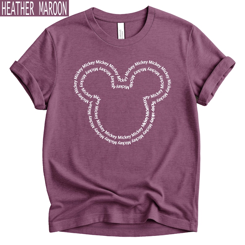 Peut inclure: T-shirt bordeaux chin&eacute; avec un motif de t&ecirc;te de Mickey Mouse blanc. La t&ecirc;te de Mickey Mouse est form&eacute;e par le mot "Mickey" r&eacute;p&eacute;t&eacute; en cercle. Le t-shirt a des manches retrouss&eacute;es.