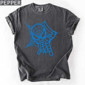 May include: Dark gray t-shirt featuring a blue graphic of a spider web and hand gesture. The word "PEPPER" is in the top left corner. The shirt has rolled-up sleeves and a crew neck.