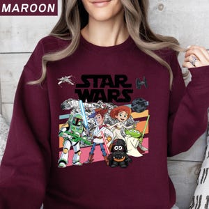 Puede incluir: Sudadera granate con un gr&aacute;fico de Star Wars con varios personajes y el logotipo de Star Wars. El gr&aacute;fico incluye a Boba Fett, Woody y Darth Vader. La sudadera tiene cuello redondo y mangas largas.