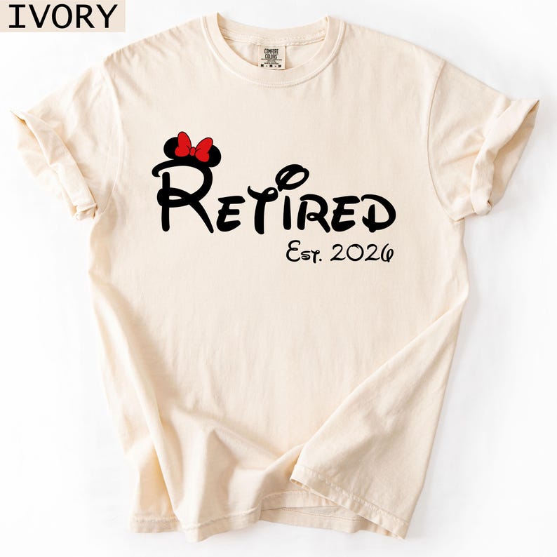 Puede incluir: Camiseta de color marfil con la palabra "Retired" en una fuente caprichosa, acompa&ntilde;ada de "Est. 2026". Una silueta negra de la cabeza de Minnie Mouse con un lazo rojo est&aacute; encima de la palabra "Retired".