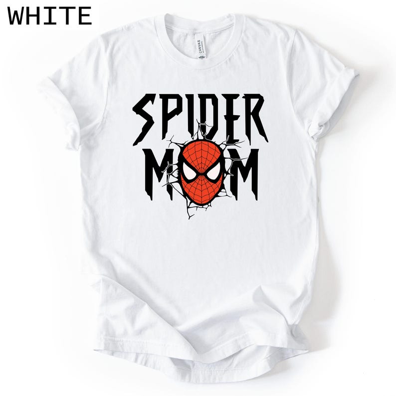 May include: White t-shirt featuring the text "SPIDER MOM" in black, with a red and black spider-themed graphic. The graphic includes a spider mask design. The word "WHITE" is in the top left corner.