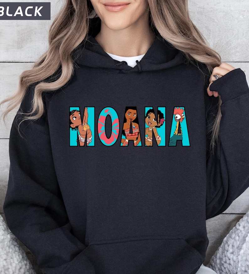 May include: Black hooded sweatshirt featuring the word "MOANA" in turquoise and coral lettering. The letters are filled with cartoon illustrations of characters from the film. The word "BLACK" is in a white box in the upper left corner.