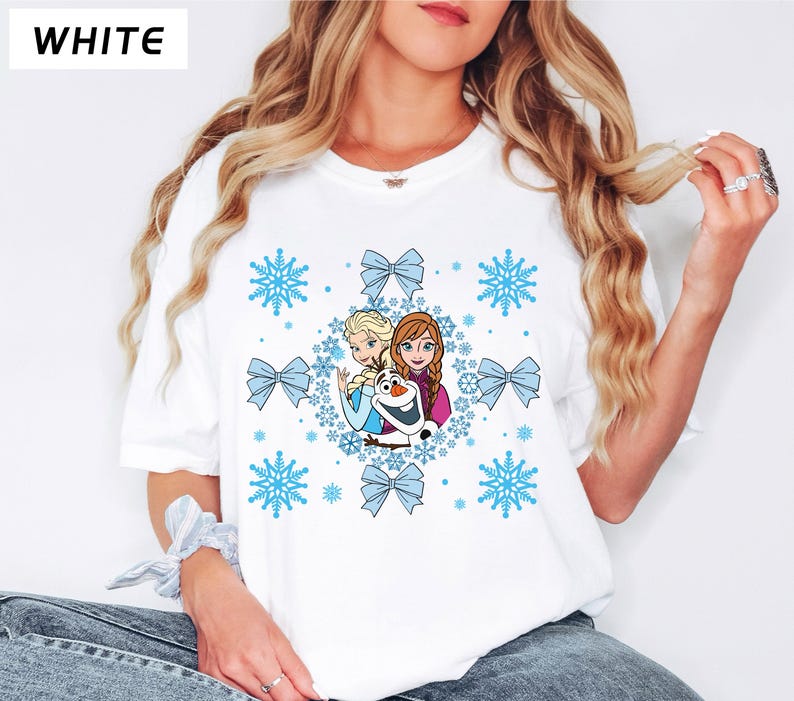 May include: White t-shirt featuring a colorful graphic of characters from the movie Frozen, including Elsa, Anna, and Olaf, surrounded by blue snowflakes and bows. The word "WHITE" is printed in the upper left corner.