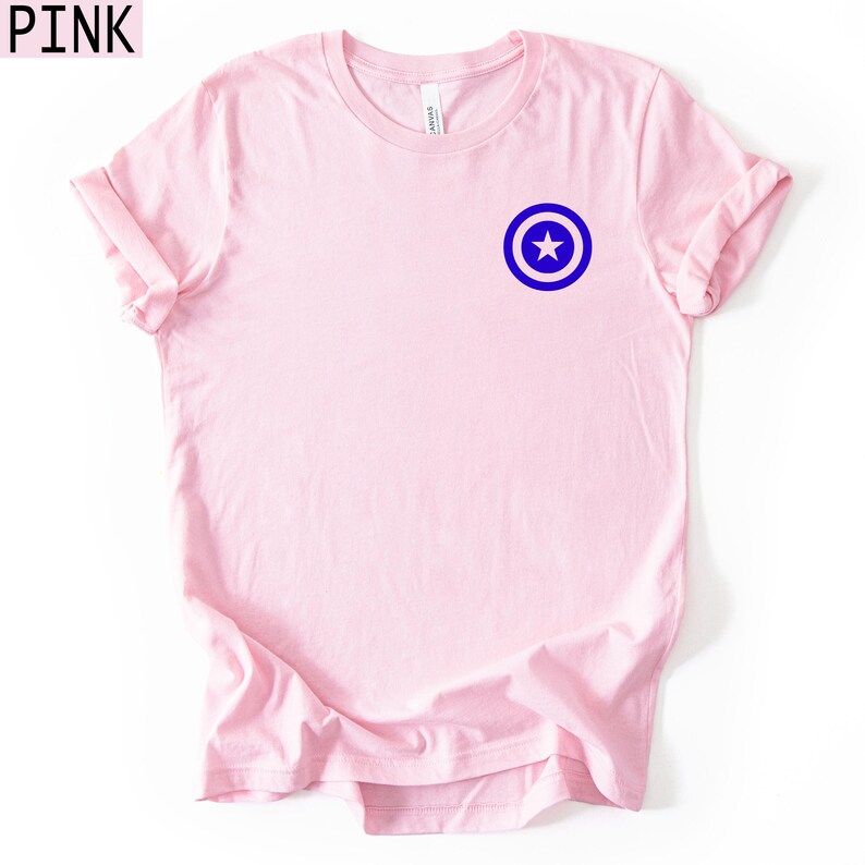 Pu&ograve; includere: T-shirt rosa chiaro con grafica blu e bianca di una stella dentro un cerchio sul petto. La parola "PINK" &egrave; nell'angolo in alto a sinistra.