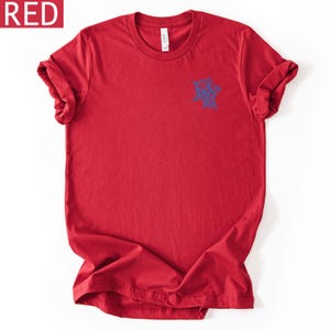 Op de afbeelding: Een rood T-shirt met korte mouwen en een ronde hals, voorzien van een kleine blauwe afbeelding van een spinnenweb op de linkerborst. Het shirt heeft een standaard pasvorm met opgerolde mouwen en een label aan de binnenkant van de hals.