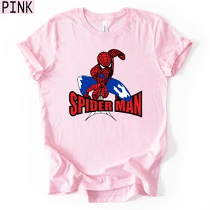 Op de afbeelding: Lichtroze t-shirt met een afbeelding van Spider-Man in rood en blauw, en de woorden "SPIDER-MAN" in rood en zwart. Het shirt heeft korte mouwen en een ronde hals.