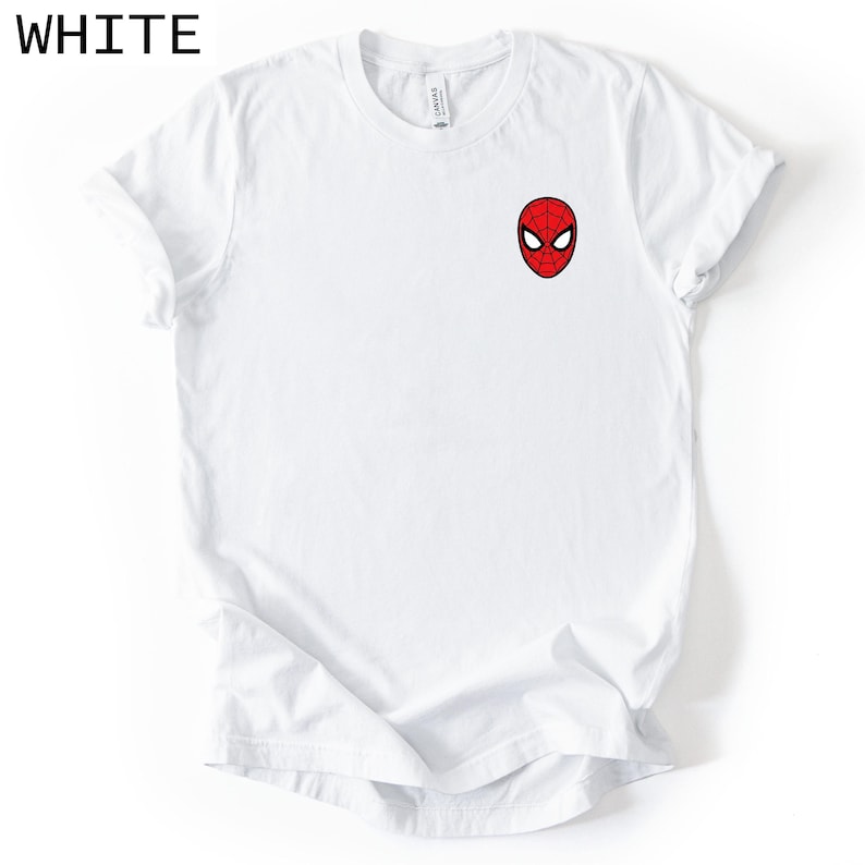 Puede incluir: Camiseta blanca con una peque&ntilde;a m&aacute;scara de Spider-Man bordada en el pecho. La m&aacute;scara es roja con telara&ntilde;as negras y ojos blancos. La palabra "WHITE" est&aacute; impresa en negro en la esquina superior izquierda. Una camiseta casual para el d&iacute;a a d&iacute;a.