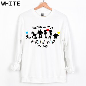 Puede incluir: Sudadera blanca con la frase "YOU'VE GOT A FRIEND IN ME" y siluetas de personajes de dibujos animados. El dise&ntilde;o incluye un perro, un caballo, Buzz Lightyear, Woody, Jessie y un extraterrestre. La palabra "WHITE" est&aacute; en la esquina superior izquierda.