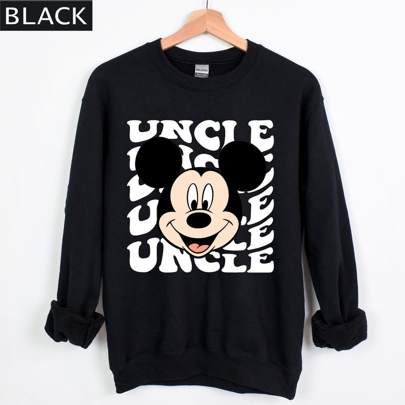 Pu&ograve; includere: Felpa nera con il volto sorridente di Topolino e la parola "UNCLE" in un motivo ripetuto. L'indumento &egrave; esposto su una gruccia di legno su sfondo bianco. La parola "BLACK" si trova nell'angolo in alto a sinistra.