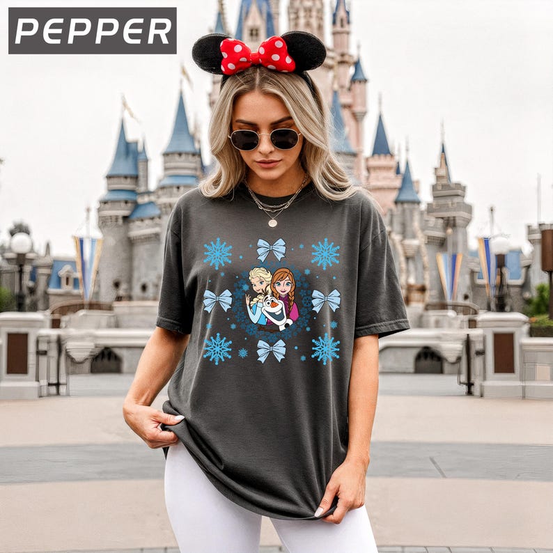 May include: Dark gray t-shirt featuring a graphic of characters from the movie Frozen, surrounded by snowflakes and bows. The word "PEPPER" is in the upper left corner. The person is wearing a Minnie Mouse ear headband and sunglasses.