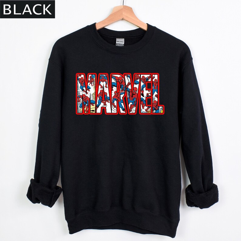 Puede incluir: Sudadera negra con la palabra "MARVEL" en letras rojas con contorno. Las letras est&aacute;n rellenas de im&aacute;genes de Spider-Man en rojo y azul. La sudadera tiene mangas largas y cuello redondo.