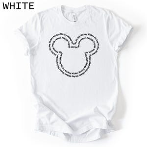 Peut inclure: T-shirt blanc avec un motif de t&ecirc;te de Mickey Mouse noir. La t&ecirc;te est form&eacute;e par le mot "Mickey" r&eacute;p&eacute;t&eacute; en cercle. Le mot "WHITE" est imprim&eacute; dans le coin sup&eacute;rieur gauche.