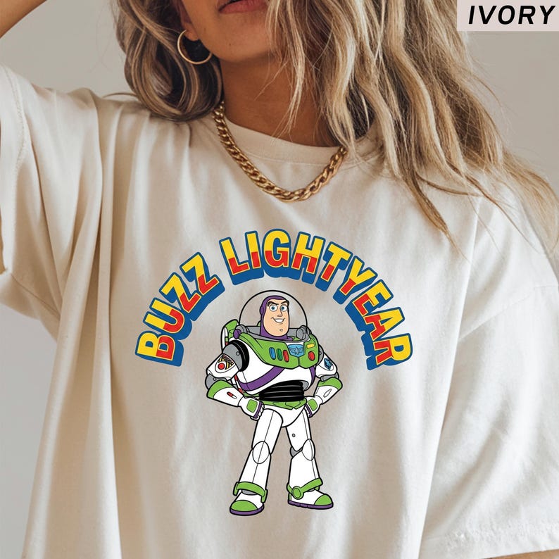 Op de afbeelding: Ivoor kleurig T-shirt met een kleurrijke afbeelding van Buzz Lightyear uit Toy Story. Het ontwerp bevat de afbeelding van het personage en de woorden "Buzz Lightyear" in een levendig, gebogen lettertype. Het shirt is een casual, comfortabele stijl.