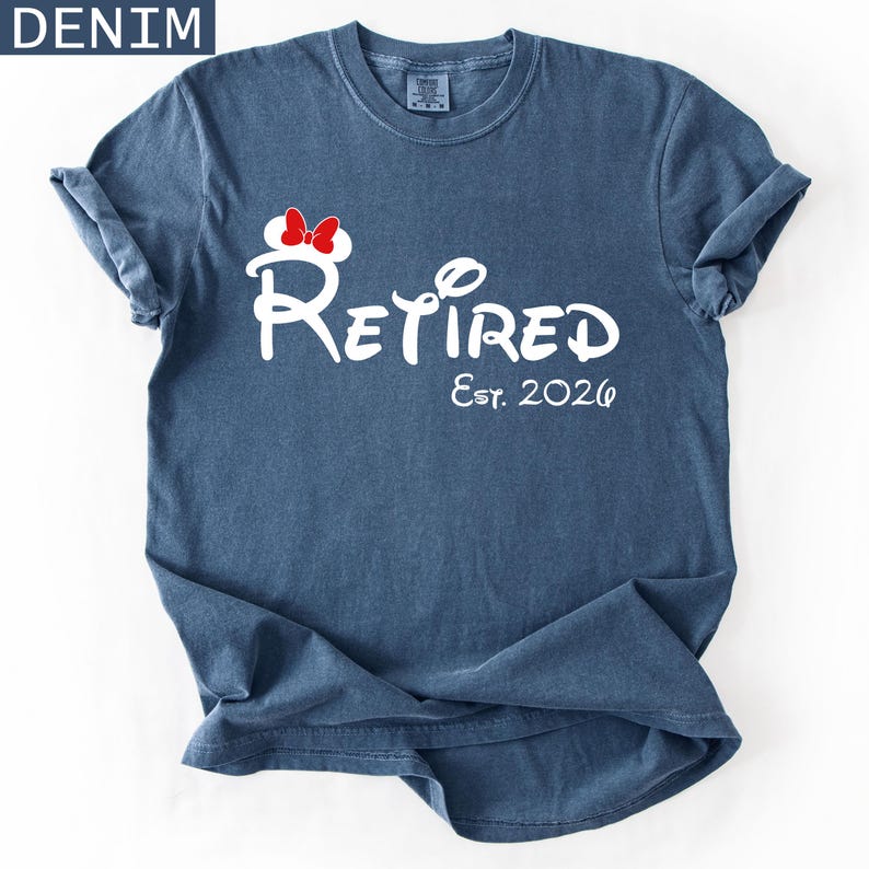 Puede incluir: Camiseta azul denim con mangas enrolladas. La camiseta presenta la palabra "Retired" en una fuente estilizada, con un lazo rojo y el texto "Est. 2026" en blanco. La palabra "DENIM" est&aacute; en un cuadro azul en la esquina superior izquierda.