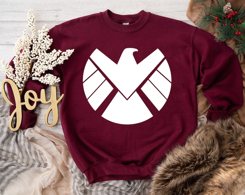 Puede incluir: Sudadera color burdeos con un gr&aacute;fico blanco del logotipo de S.H.I.E.L.D.