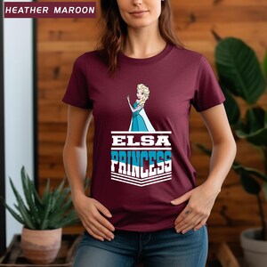 May include: Heather maroon t-shirt featuring a graphic of Elsa from Frozen, with the text "ELSA PRINCESS" in white and blue. The shirt has a crew neck and short sleeves. The top left corner of the image has the text "HEATHER MAROON".