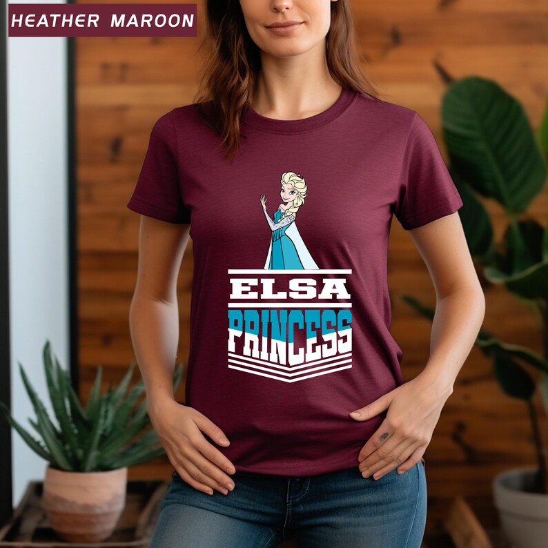 May include: Heather maroon t-shirt featuring a graphic of Elsa from Frozen, with the text "ELSA PRINCESS" in white and blue. The shirt has a crew neck and short sleeves. The top left corner of the image has the text "HEATHER MAROON".