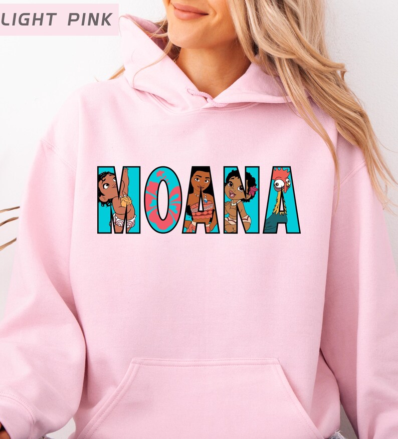 May include: Pale pink hoodie featuring the word "MOANA" in a colourful graphic design. The letters incorporate cartoon characters from the film. The hoodie has a front pocket and a hood.