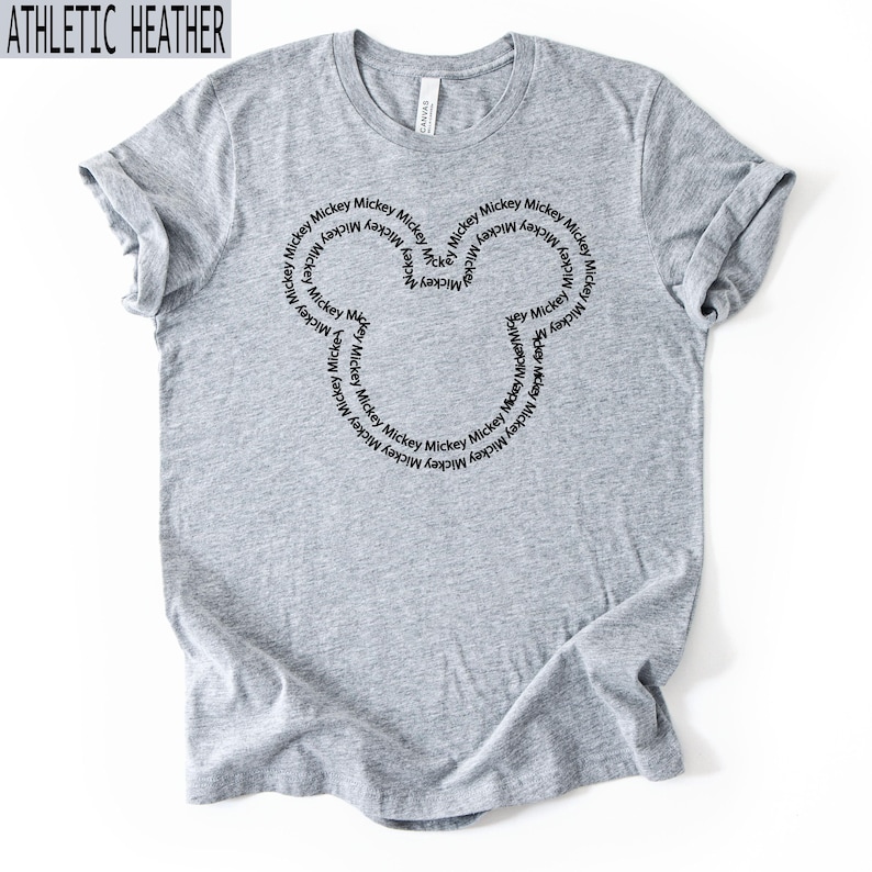 Peut inclure: T-shirt gris chin&eacute; avec un motif de t&ecirc;te de Mickey Mouse noir. La t&ecirc;te de Mickey Mouse est form&eacute;e par le mot "Mickey" r&eacute;p&eacute;t&eacute; en cercle. Le t-shirt est fait d'une mati&egrave;re douce et confortable.