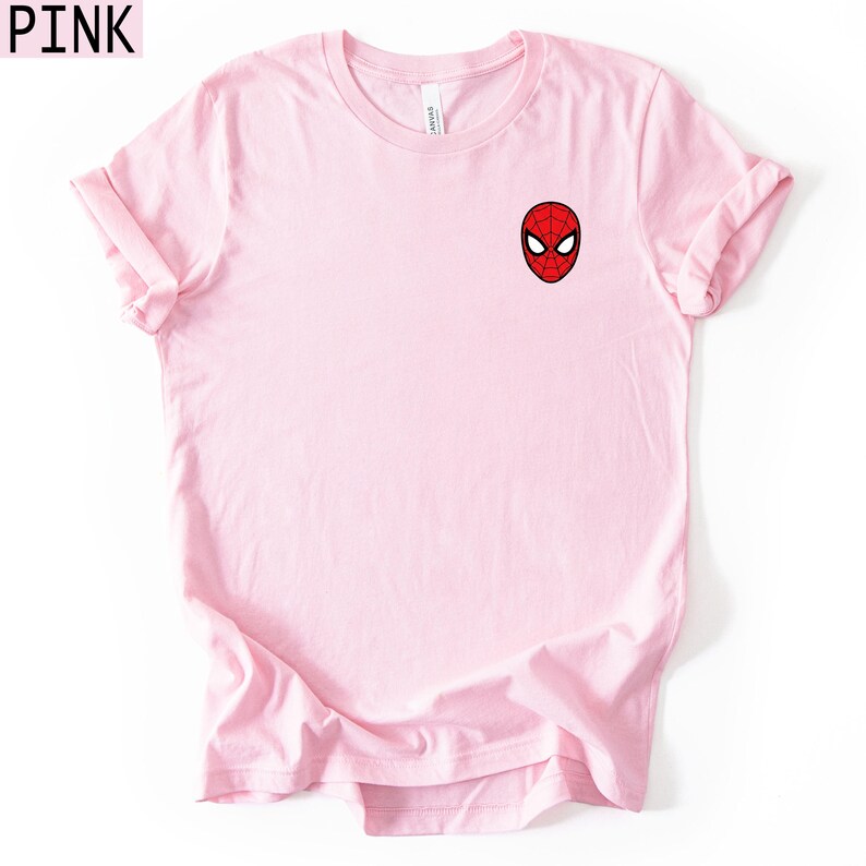 Puede incluir: Una camiseta rosa claro con una peque&ntilde;a m&aacute;scara de Spider-Man bordada en rojo, negro y blanco. La camiseta tiene mangas cortas y cuello redondo. La palabra "PINK" est&aacute; en la esquina superior izquierda.
