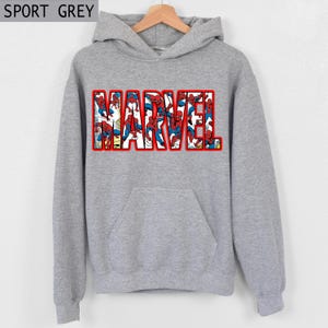 Puede incluir: Sudadera gris con la palabra "MARVEL" en letras grandes con contorno rojo. Las letras est&aacute;n rellenas de im&aacute;genes de Spider-Man con su cl&aacute;sico traje rojo y azul. La sudadera tiene un bolsillo delantero y una capucha con cord&oacute;n. El texto "SPORT GREY" est&aacute; en la esquina superior izquierda.