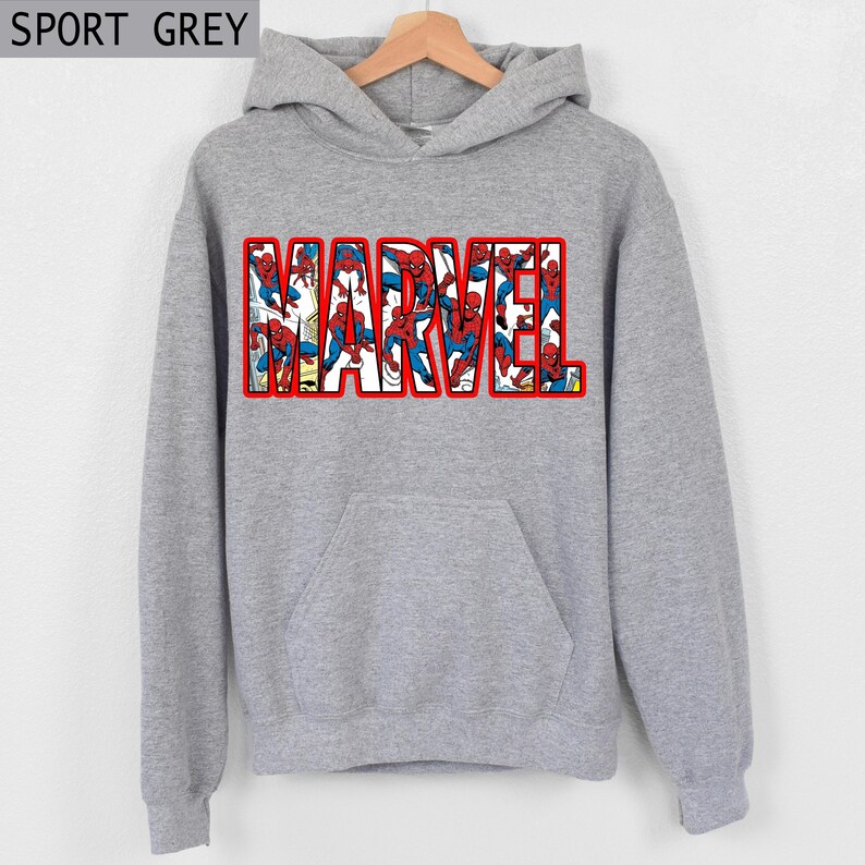 Puede incluir: Sudadera gris con la palabra "MARVEL" en letras grandes con contorno rojo. Las letras est&aacute;n rellenas de im&aacute;genes de Spider-Man con su cl&aacute;sico traje rojo y azul. La sudadera tiene un bolsillo delantero y una capucha con cord&oacute;n. El texto "SPORT GREY" est&aacute; en la esquina superior izquierda.