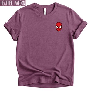 Puede incluir: Camiseta color granate jaspeado con un peque&ntilde;o gr&aacute;fico de la cara de Spider-Man en el pecho. La camiseta de manga corta tiene las mangas enrolladas y cuello redondo. El texto "HEATHER MAROON" est&aacute; en la esquina superior izquierda.