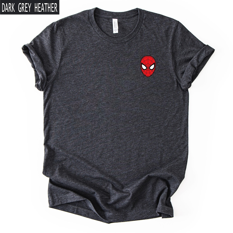 Puede incluir: Camiseta gris oscuro jaspeado con un peque&ntilde;o gr&aacute;fico de m&aacute;scara de Spider-Man roja y negra en el pecho. La camiseta tiene mangas cortas y cuello redondo. El texto "DARK GREY HEATHER" est&aacute; en un cuadro blanco en la esquina superior izquierda.
