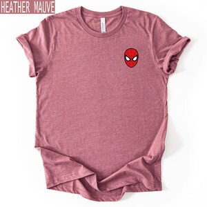 Puede incluir: Camiseta color malva jaspeado con un peque&ntilde;o gr&aacute;fico de la m&aacute;scara de Spider-Man en el pecho. La camiseta es de color liso y tiene cuello redondo. El texto "HEATHER MAUVE" est&aacute; en un recuadro en la esquina superior izquierda.